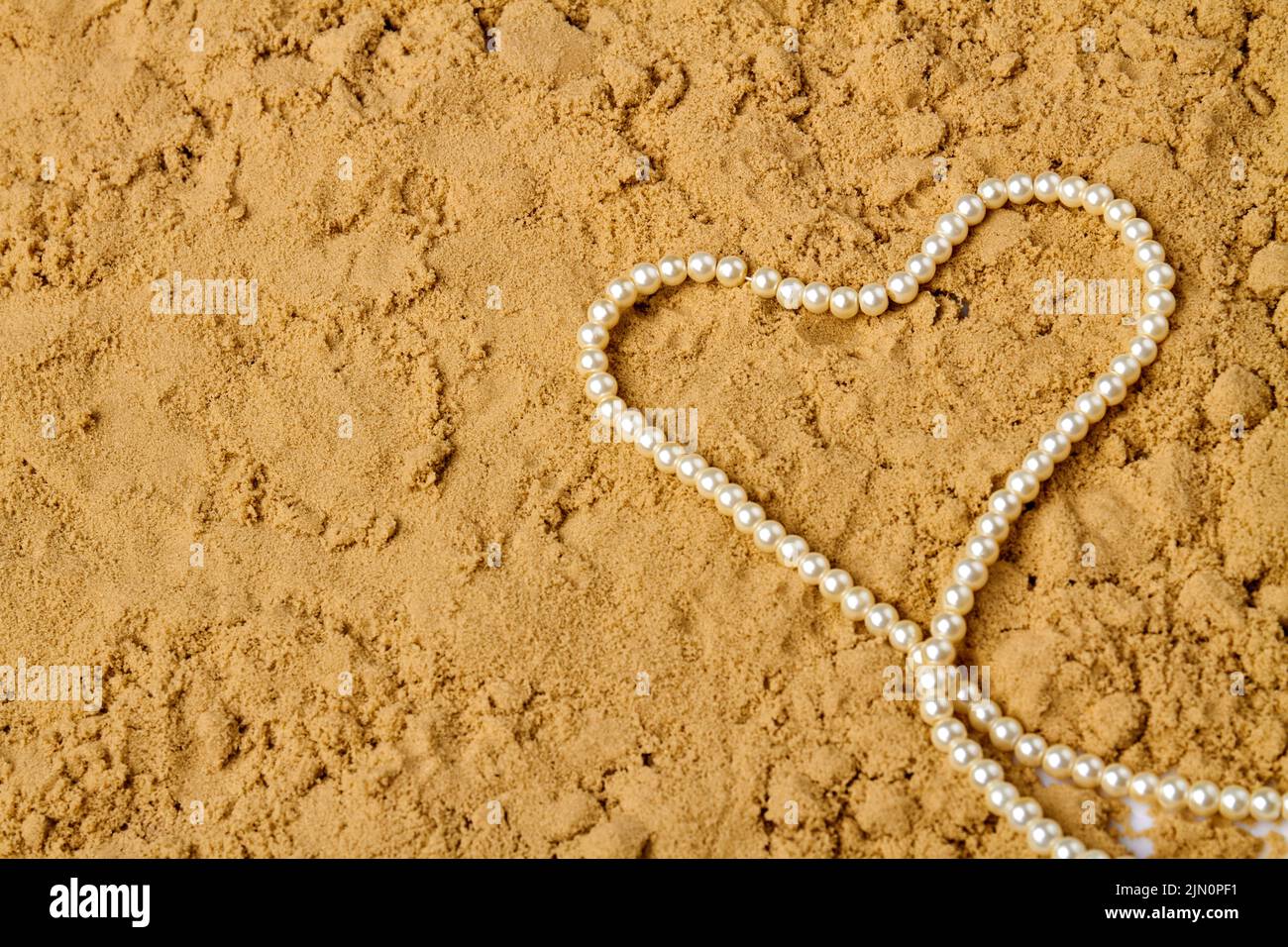 Corazón hecho de perlas blancas sobre arena húmeda. Espacio de copia de la vista superior. Foto de stock