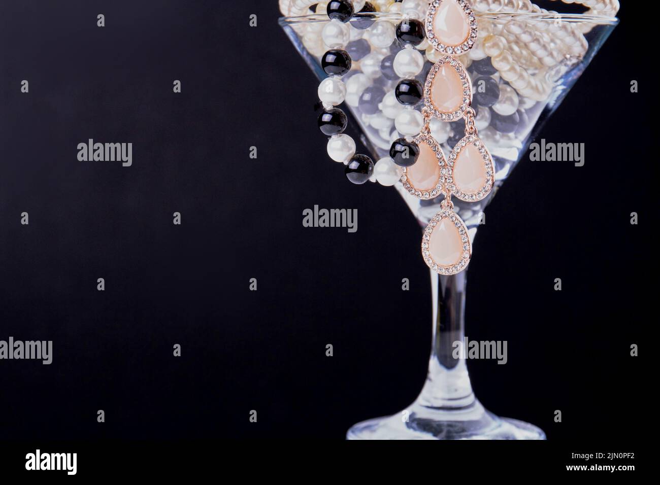 Primer plano copa de cóctel llena de perlas sobre fondo oscuro. Taza rellena de joyas. Foto de stock
