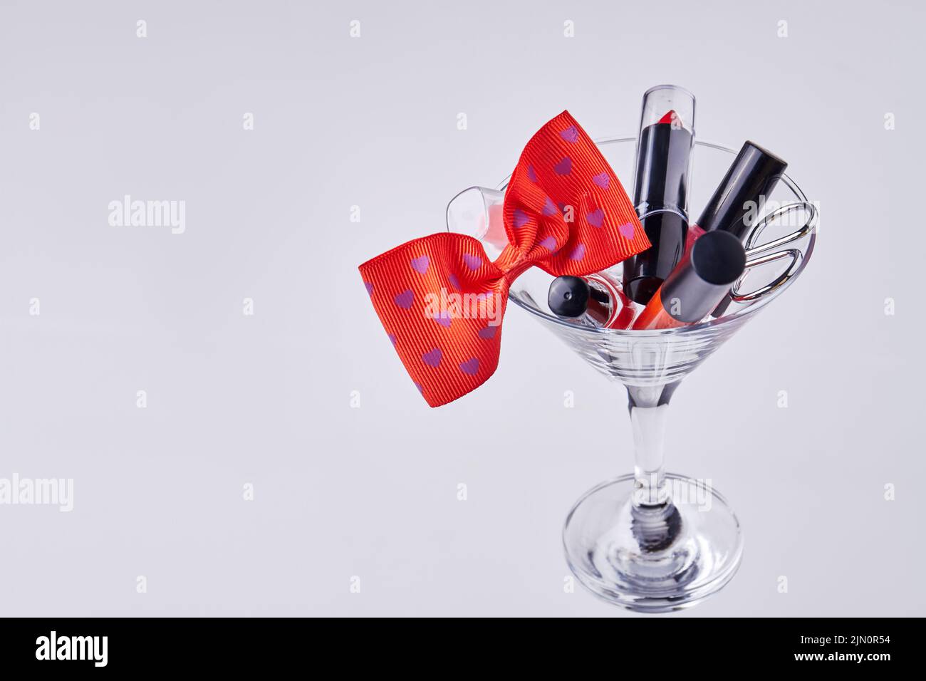 Accesorios de maquillaje y pajarita roja en copa de cóctel. Aislado sobre fondo blanco. Foto de stock