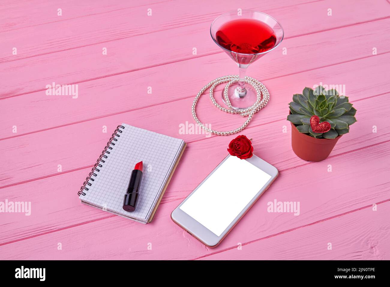 Smartphone con pantalla en blanco para espacio de copia. Vista superior de los accesorios para mujer sobre un escritorio de madera rosa. Foto de stock