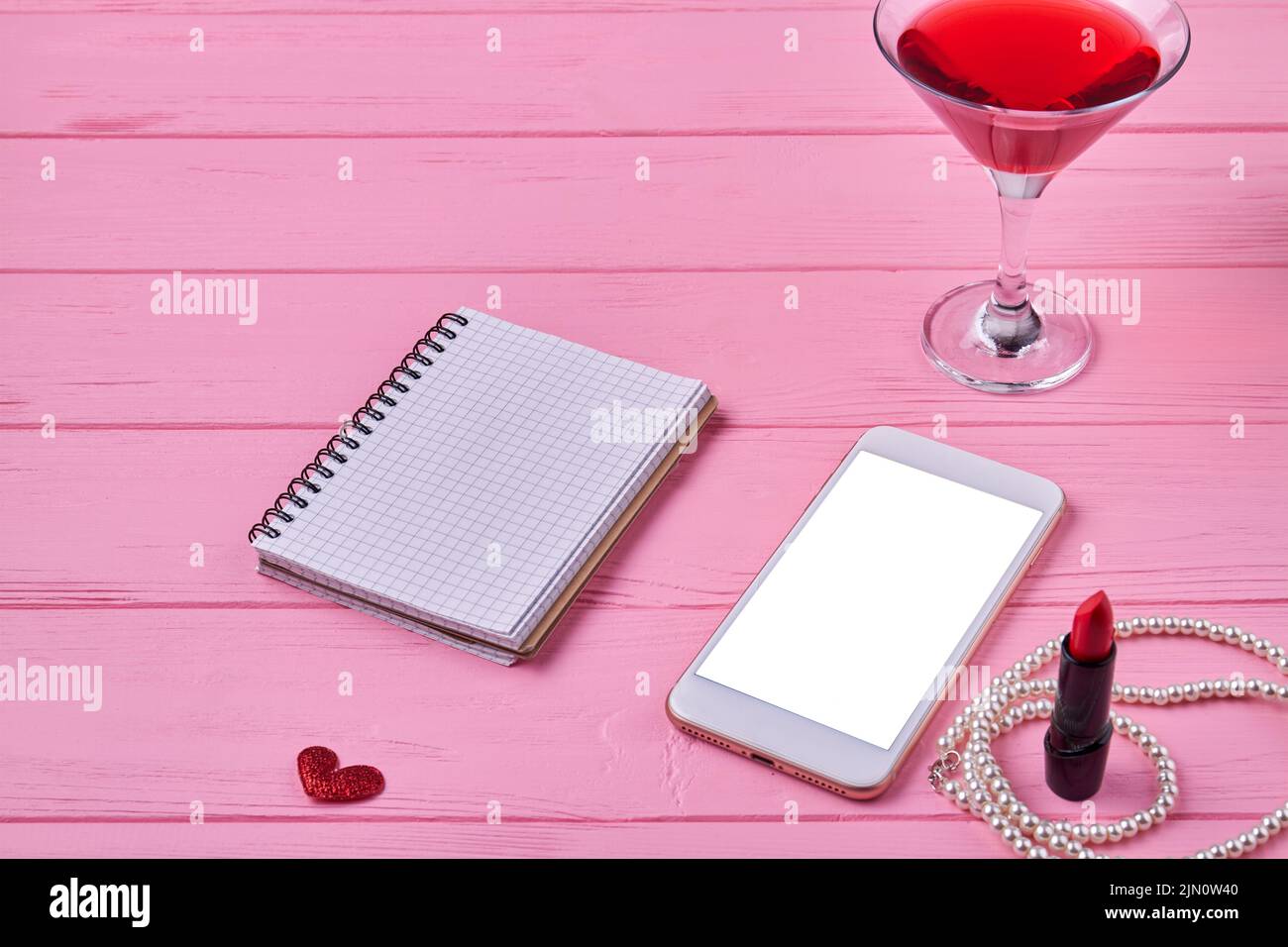 Smartphone con pantalla en blanco y bloc de notas abierto para espacio de copia. Accesorios para mujer sobre escritorio de madera rosa. Foto de stock