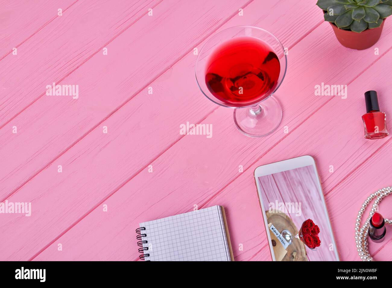 Vista superior de accesorios femeninos sobre un escritorio de madera rosa. Smartphone con bloc de notas y cóctel. Foto de stock