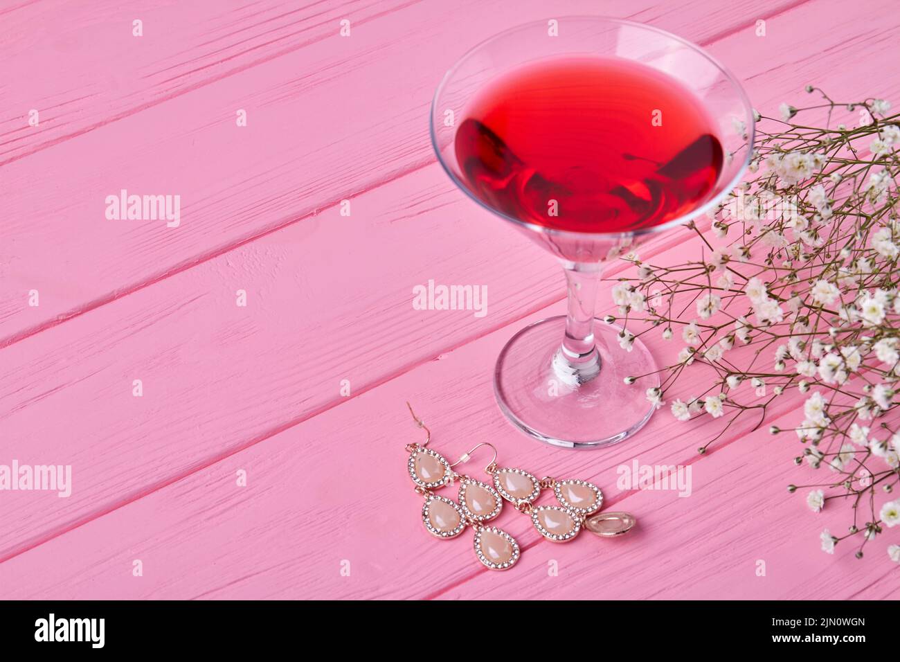 Primer plano de vaso de martini rojo con pendientes. Flores blancas diminutas. Foto de stock