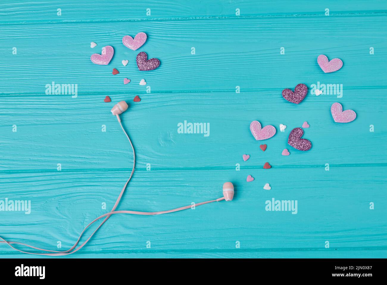 Auriculares con corazones rosas y moradas sobre madera azul. Amor por el concepto de música. Foto de stock