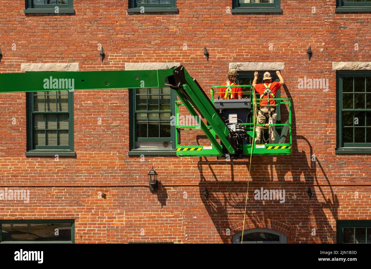 Trabajadores de la construcción instalando nuevas ventanas en un edificio de un molino en el centro de Bideford Maine Foto de stock