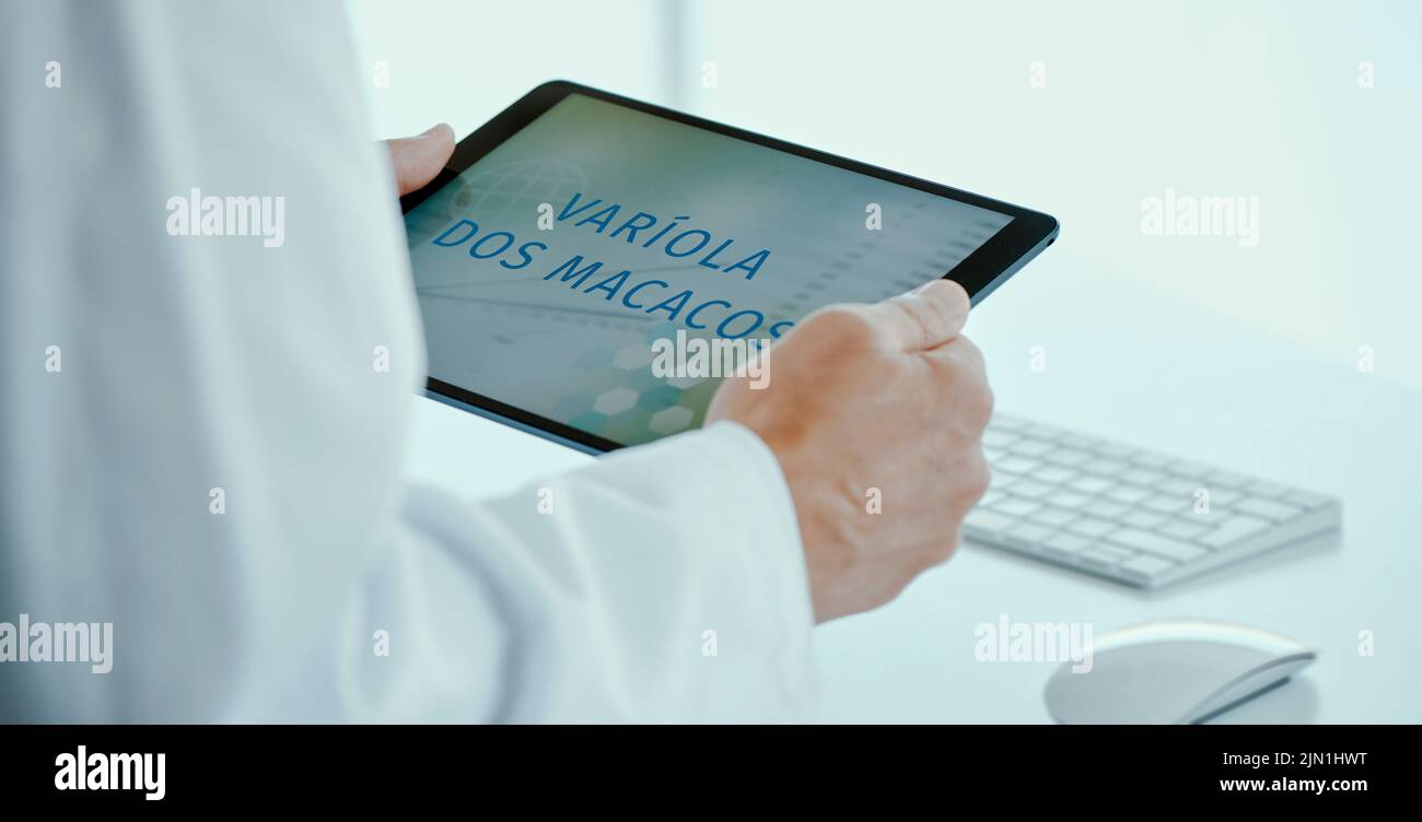 un médico hombre, en un abrigo blanco, tiene una tableta digital en sus manos con el texto monkeypox escrito en portugués en su pantalla, en un formato panorámico a. Foto de stock