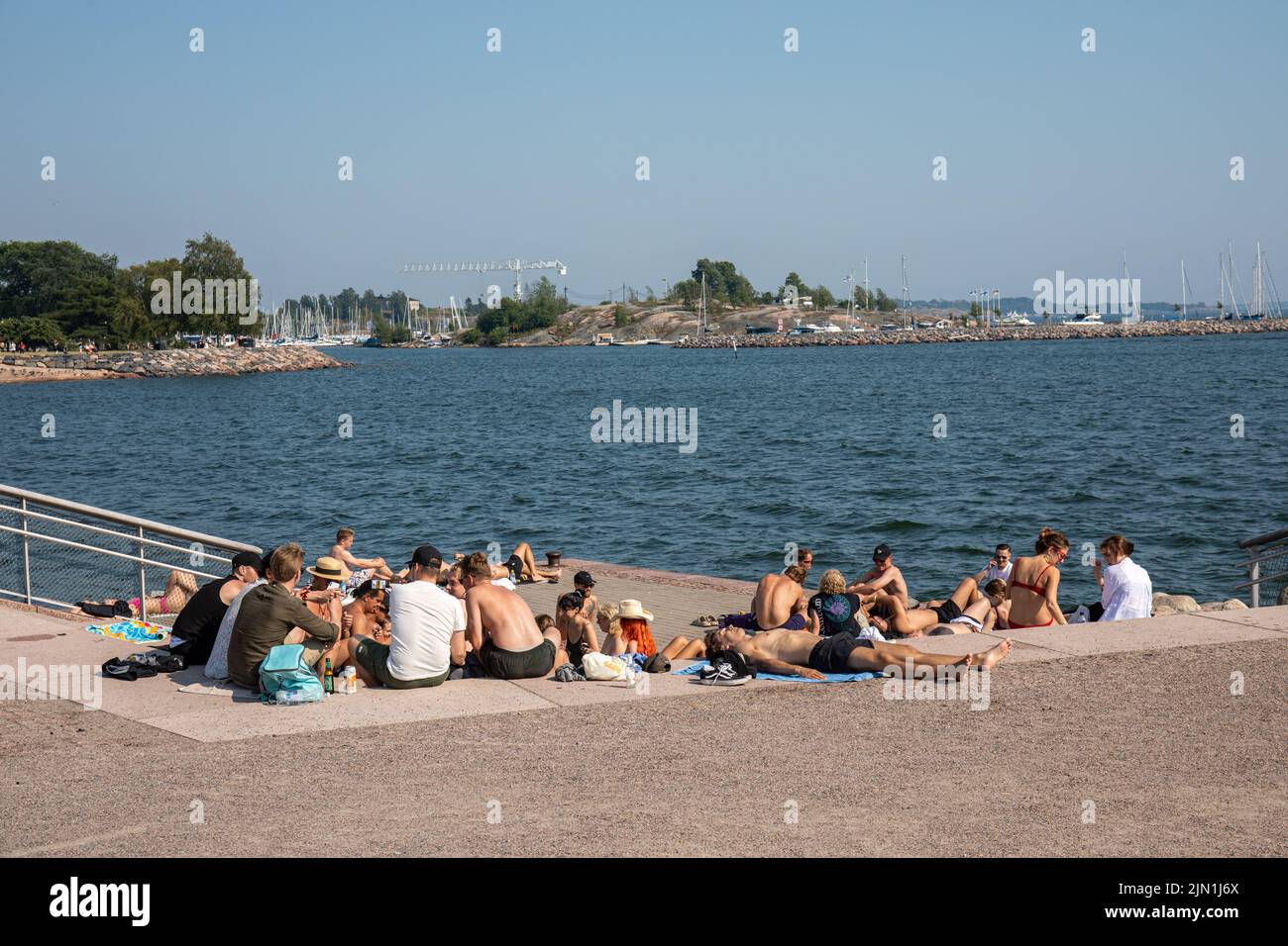 Jóvenes que pasan el rato en el puerto durante un caluroso día de verano en el distrito de Eira de Helsinki, Finlandia Foto de stock