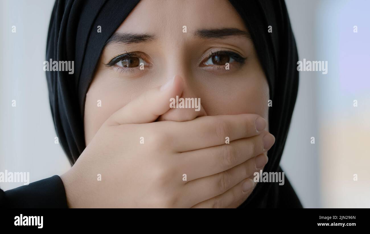 Retrato femenino en interiores chica árabe islámica triste miedo mujer musulmana dama árabe en negro hijab mirando la cámara cubre la boca con manos silencio tranquilo Foto de stock