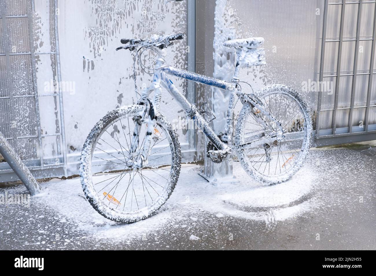 Lavar una bicicleta con un chorro de espuma en un lavado de coches. La bicicleta está cubierta de espuma. Autoservicio. Mantenimiento de bicicletas. Foto de stock