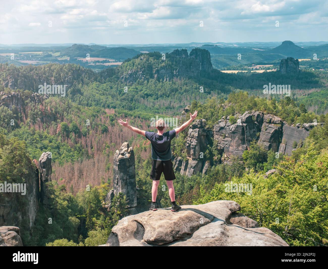 El excursionista grita saludos en el valle por debajo de la roca Carolafelsen, Grossen Dom y las montañas irregulares Schrammsteine y Falkenstein Foto de stock
