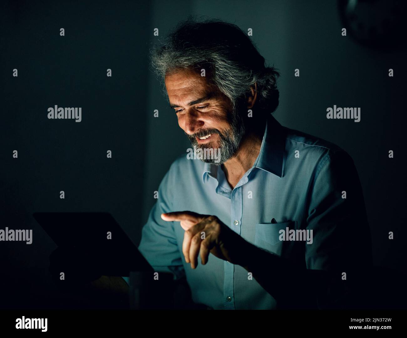 Retrato de un hombre de negocios sénior con tablet o portátil que trabaja hasta altas horas de la noche en la oficina Foto de stock