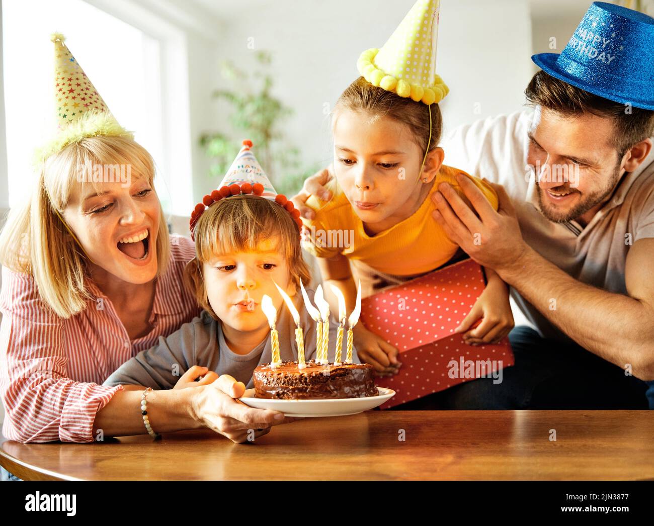Familia de cuatro, madre, padre, hija e hijo divertirse celebrando un cumpleaños junto con pastel de cumpleaños y velas y un regalo de vela blowin Foto de stock