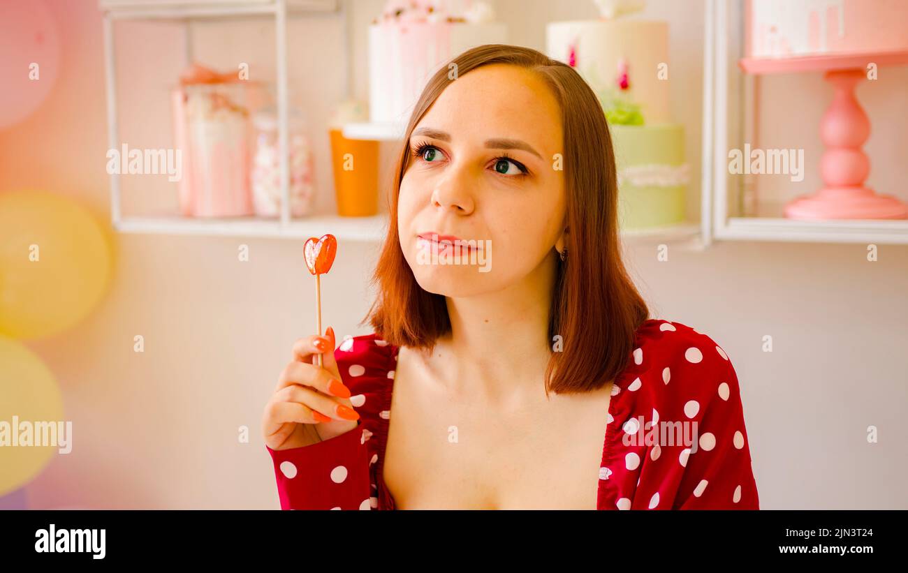 Mujer joven con el pelo corto lamer lollipop. Retrato de señora positiva vestido rojo con caramelo Foto de stock