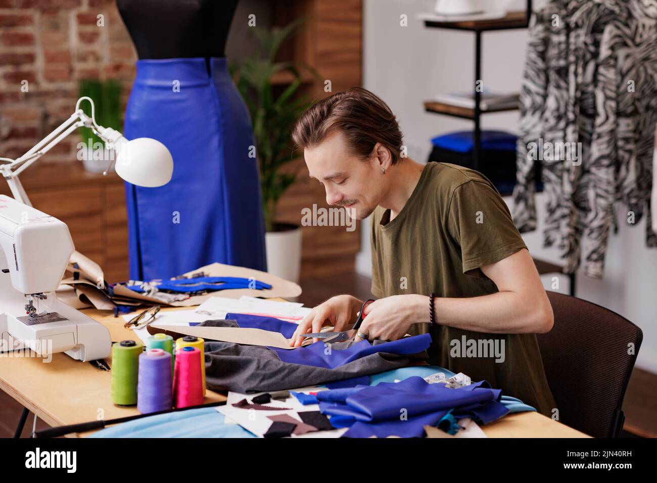 Un joven es un diseñador de moda, corte de tela para coser una nueva colección. Oficina en casa del diseñador Foto de stock