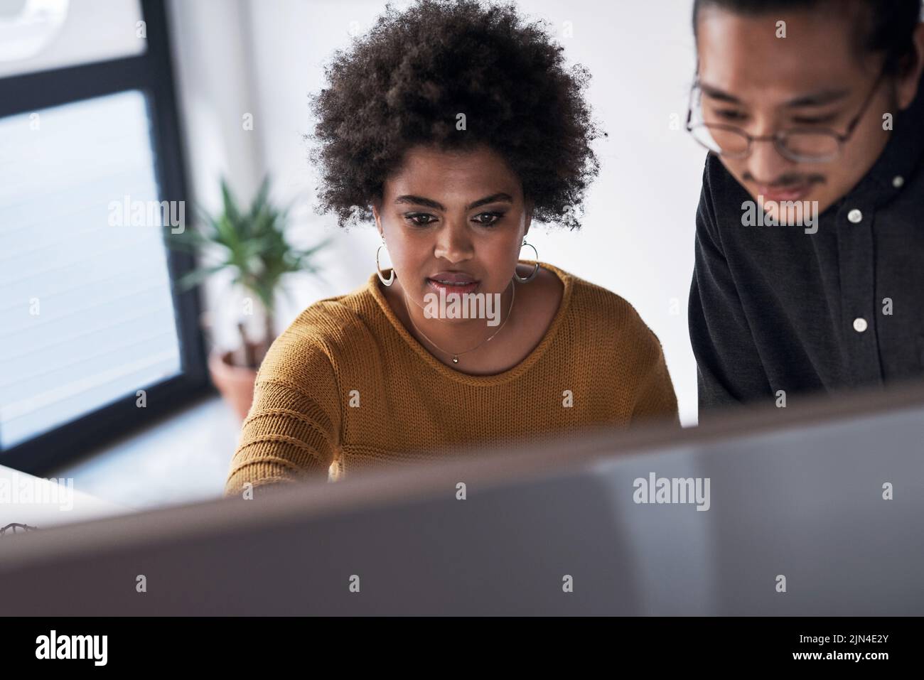 ¿Qué piensa de esto? Dos jóvenes empresarios que trabajan juntos en una computadora en la oficina durante el día. Foto de stock