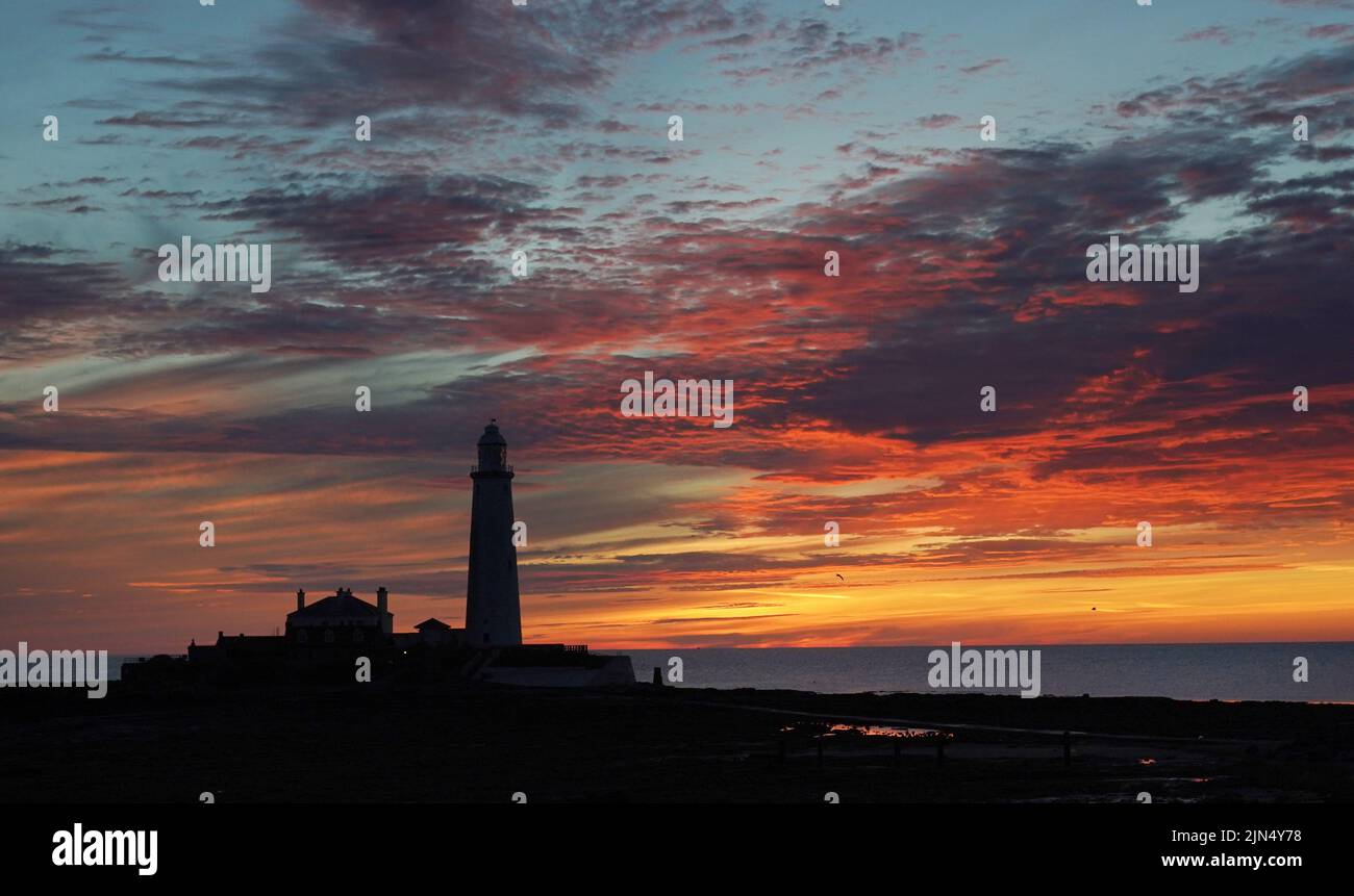 Un cielo naranja justo antes del amanecer en el faro de St Mary en Whitley Bay. Fecha de la foto: Martes 9 de agosto de 2022. Foto de stock