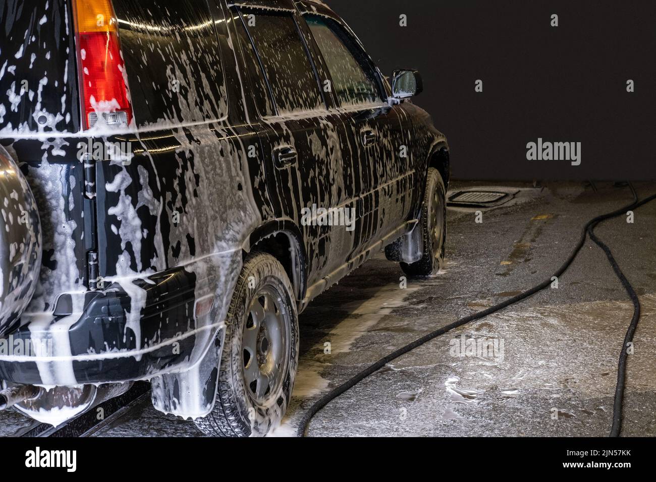 Lavado de coche negro con espuma activa. El coche es atendido en el lavabo. Autoservicio de lavado de coches. Eliminación de suciedad en el coche. Foto de stock