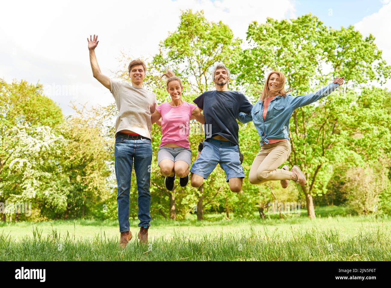 Cuatro amigos saltan en el aire juntos en un prado verde en verano Foto de stock