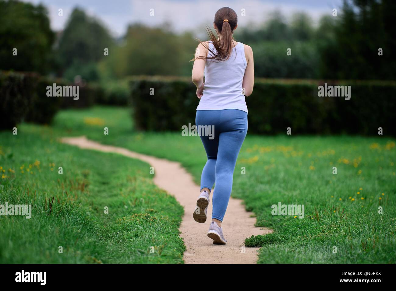 Vista posterior de una corredora haciendo ejercicio en un parque público en verano. Foto de stock