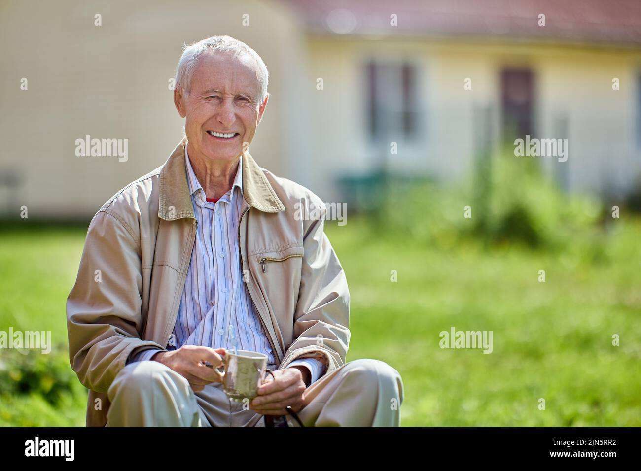 Toothy sonrisa hombre mayor de 75 años se sienta al aire libre en frente de su casa. Foto de stock