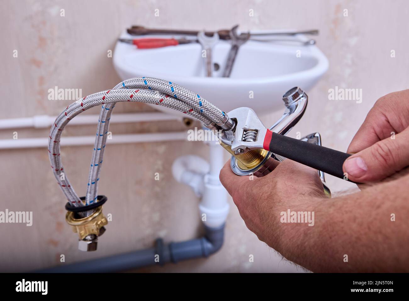 Trabajos de fontanería En el cuarto del baño, un fontanero instala un nuevo grifo de agua en el sistema de tuberías de la casa. Foto de stock