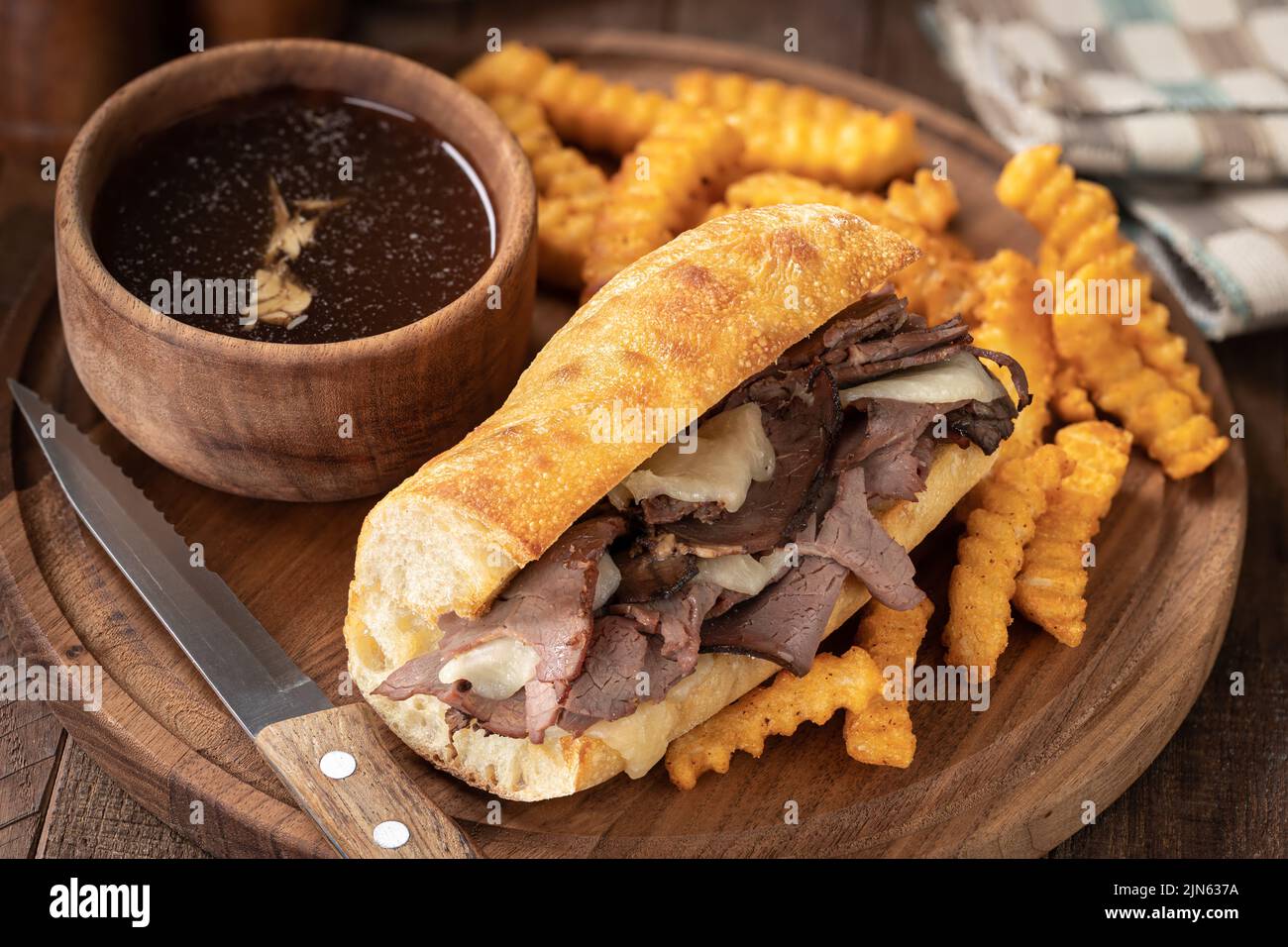 Sándwich francés y patatas fritas con un cuenco de au jus ion una fuente de madera Foto de stock
