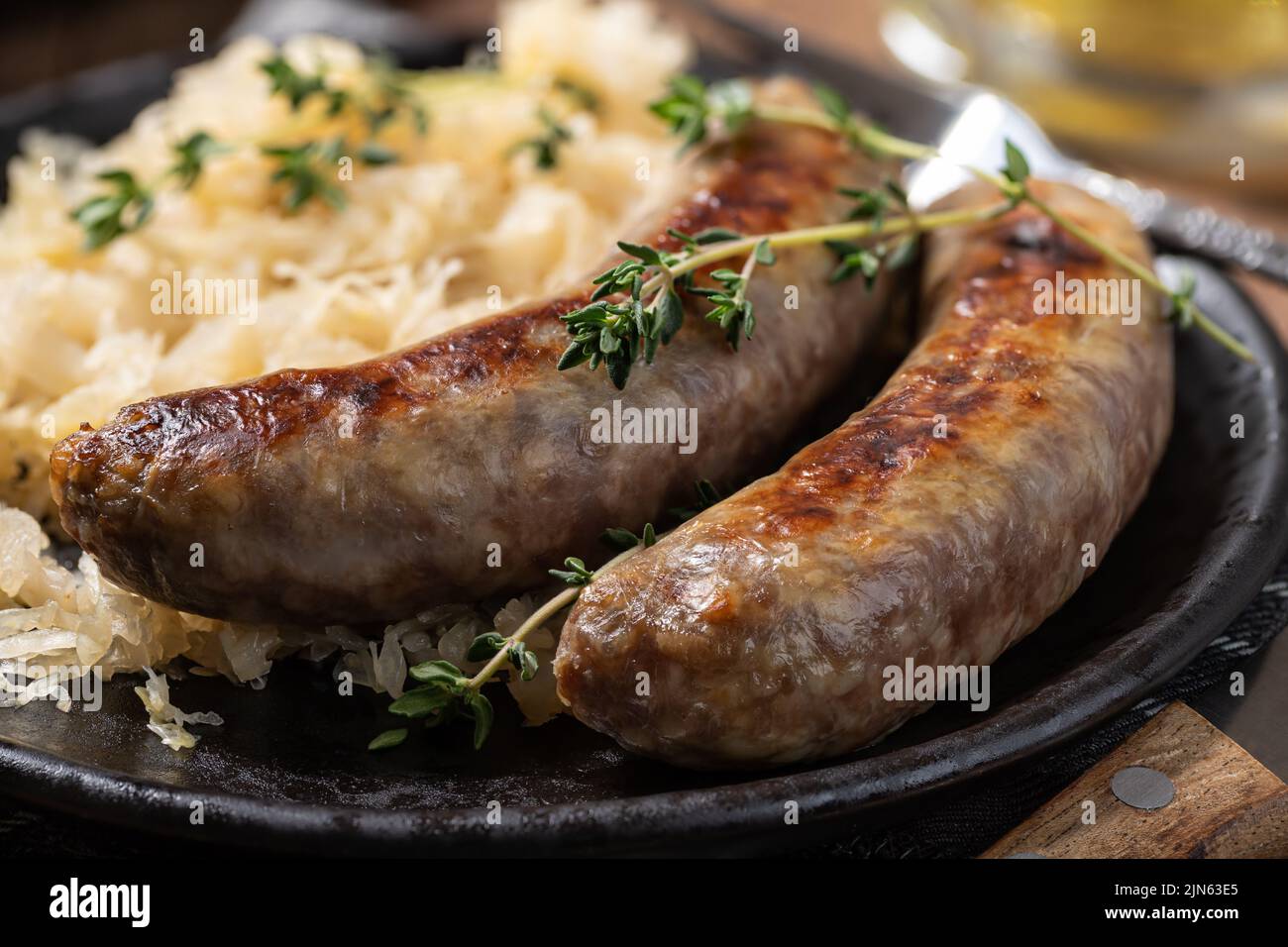 Primer plano de la cena de bratwurst con chucrut adornado con tomillo en un plato negro Foto de stock