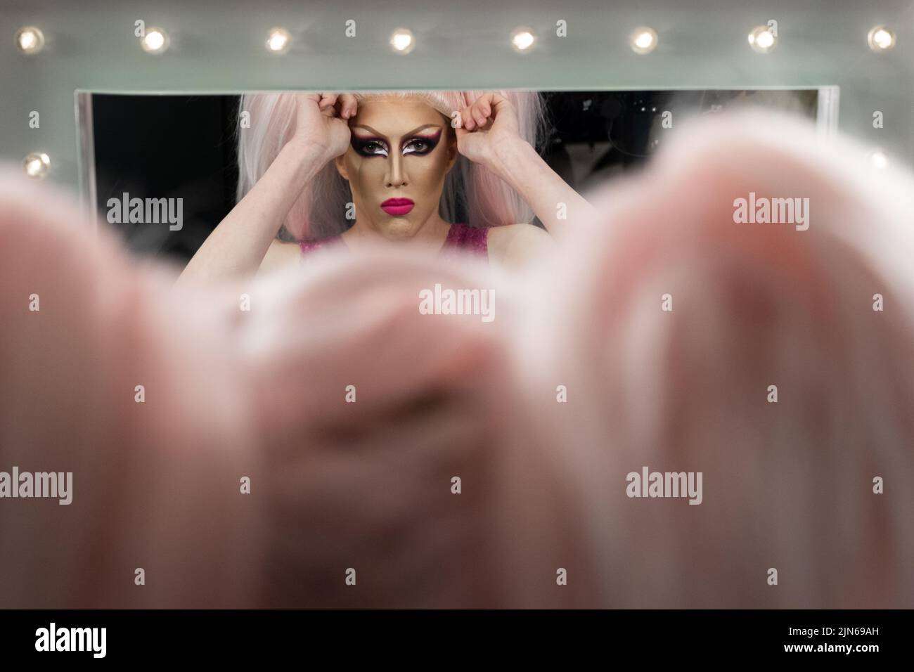 Persona no binaria aplicando maquillaje de la reina del arrastre Backstage, mirando en espejo Foto de stock