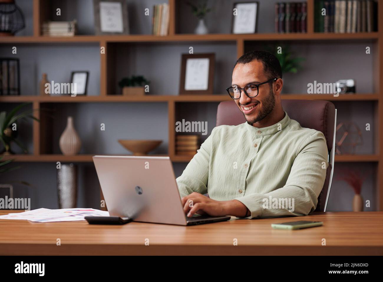 Retrato de un joven hombre de negocios africano que trabaja con un ordenador portátil en la oficina. Sonriente empresario confidente usando gafas con computadora en Foto de stock
