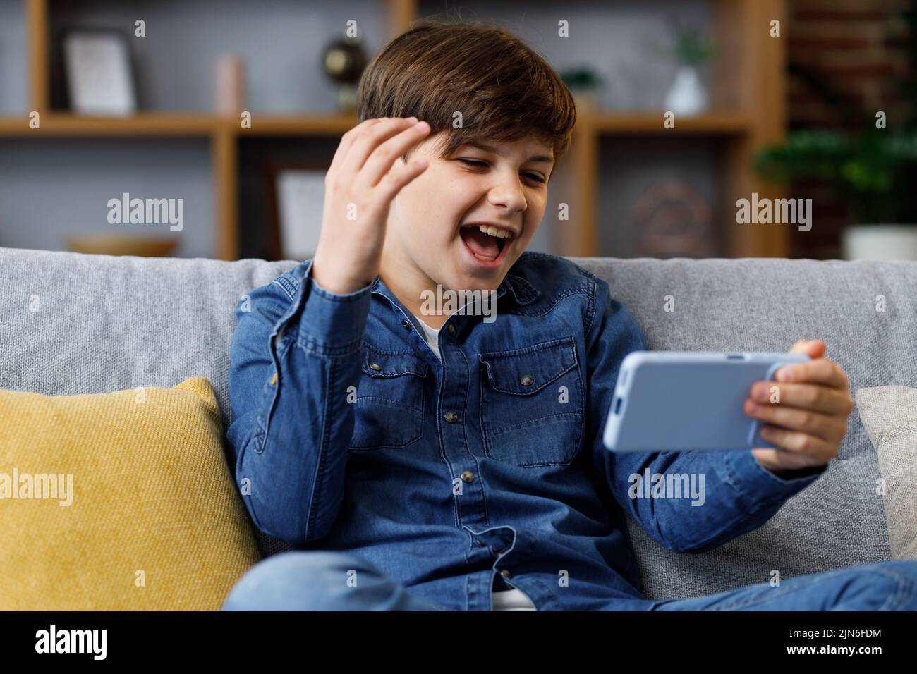 El niño reacciona emocionalmente a lo que está sucediendo en la pantalla del smartphone. Un adolescente pasa tiempo en casa con un aparato digital. Adolescencia y. Foto de stock