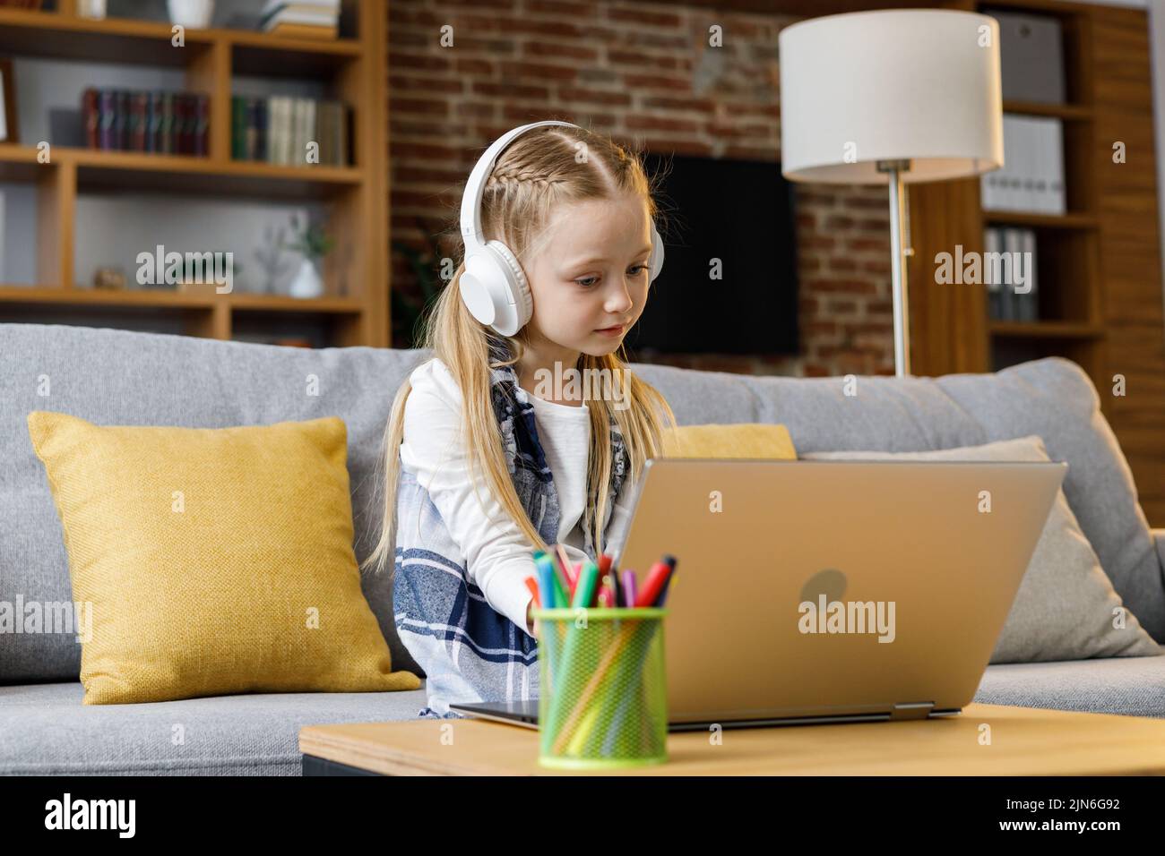 Linda niña de escuela primaria estudiando en casa usando una computadora portátil. Niño serio haciendo la tarea, contestando la pregunta en línea de la prueba, pasando el examen Foto de stock