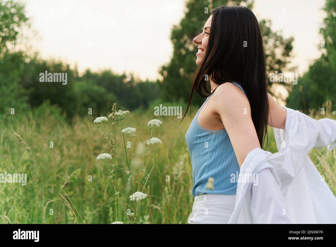 Mujer joven sonriente en camisa blanca disfrutando de la naturaleza en Green Meadow Foto de stock
