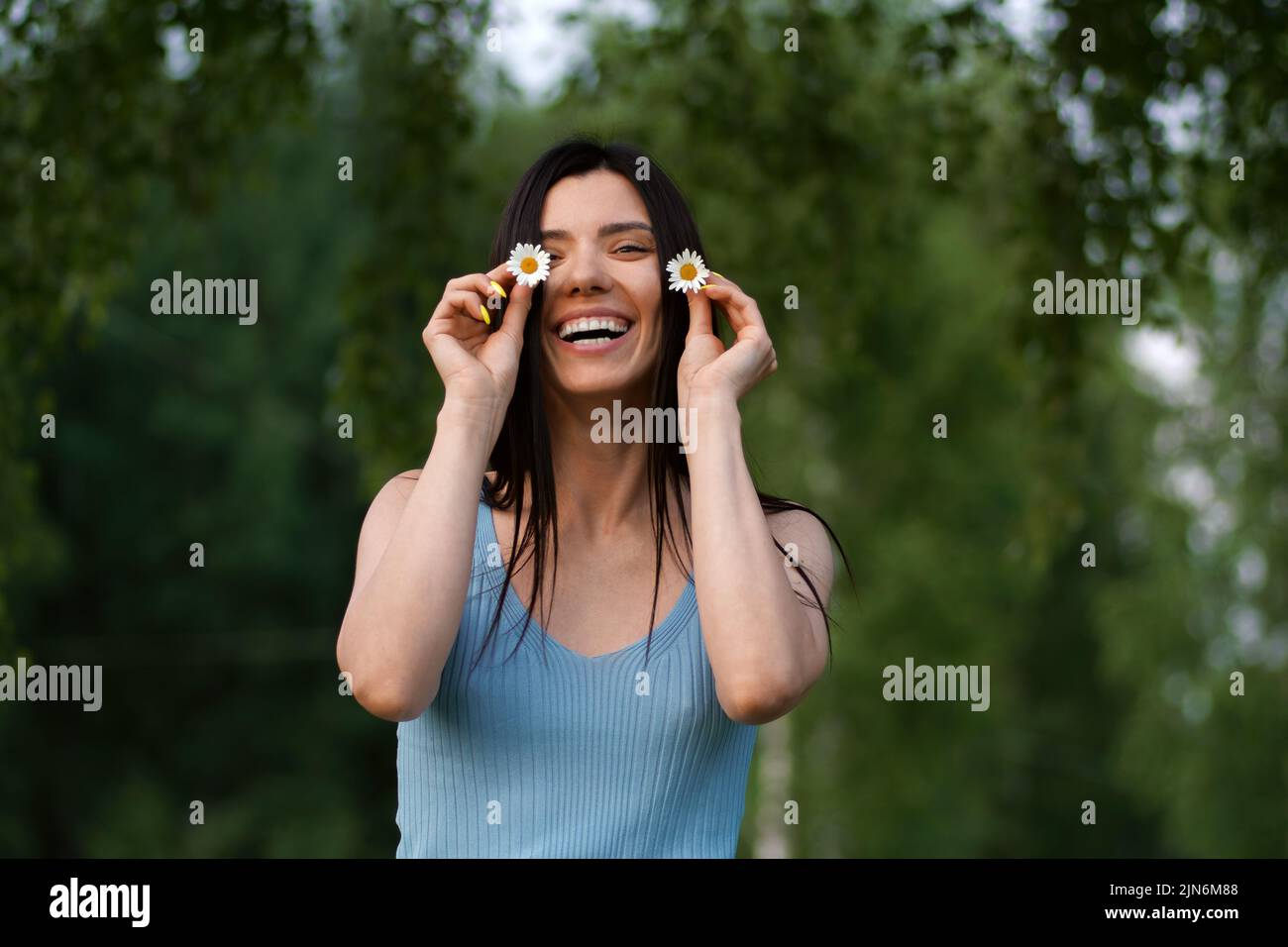 Hermosa joven mujer sonriendo y sosteniendo margaritas. Retrato brillante Foto de stock