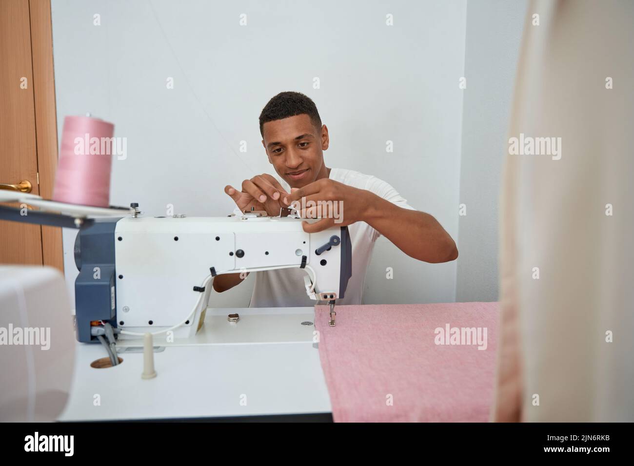 Smiling joven sastre disfrutando el trabajo en atelier con equipo Foto de stock