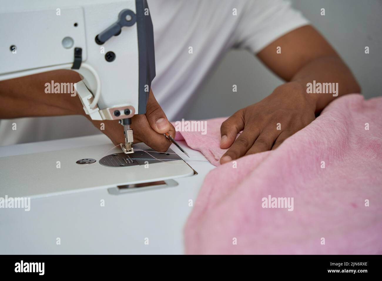 Hombre cosiendo ropa con equipo profesional en su propio taller Foto de stock
