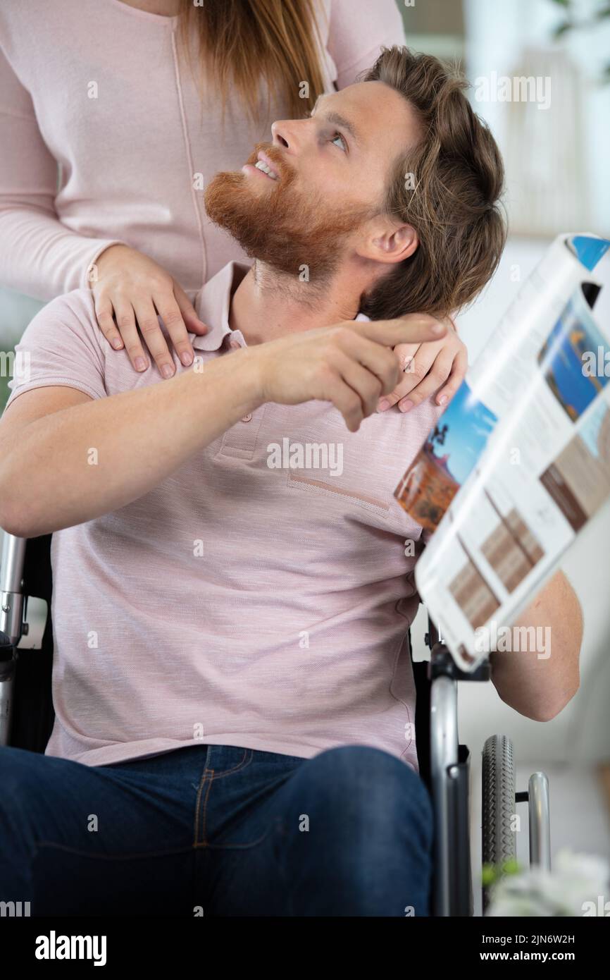 hombre leyendo un libro en silla de ruedas con su esposa Foto de stock