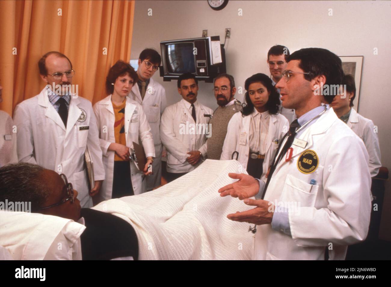 Anthony Fauci durante los primeros años de la epidemia de SIDA Dr. Anthony Fauci y equipo de tratamiento con un paciente de SIDA temprano en NIH durante rondas médicas, alrededor de 1986. Crédito: NIAID Foto de stock