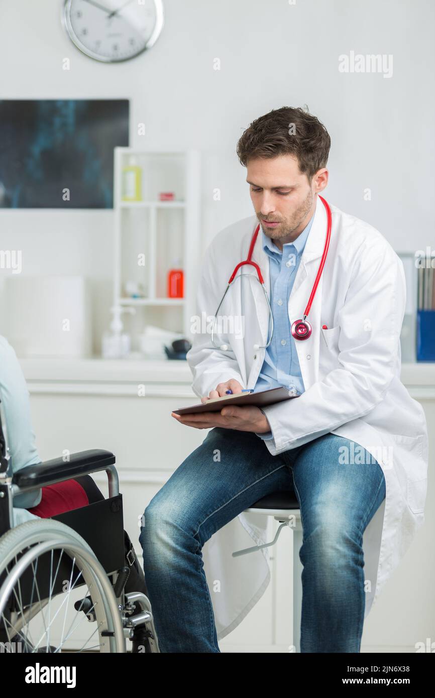 el médico que escribe en el consultorio con un paciente discapacitado Foto de stock
