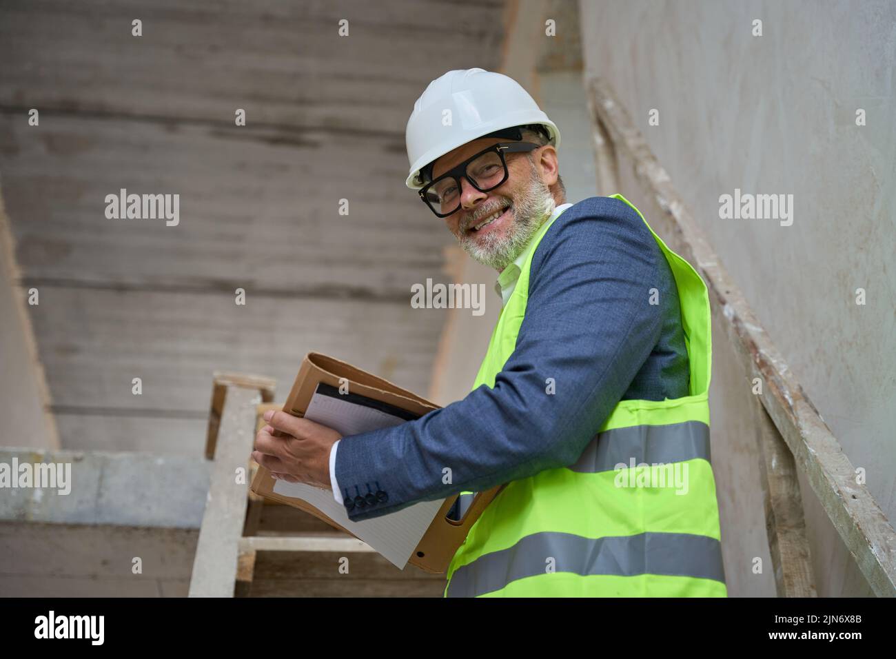 Hombre sonriente capataz sosteniendo una carpeta mientras estaba de pie en las escaleras de la cabaña Foto de stock