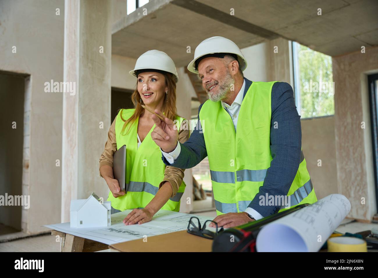sonriendo agente inmobiliario y capataz inspeccionando la casa de pie cerca de la mesa Foto de stock
