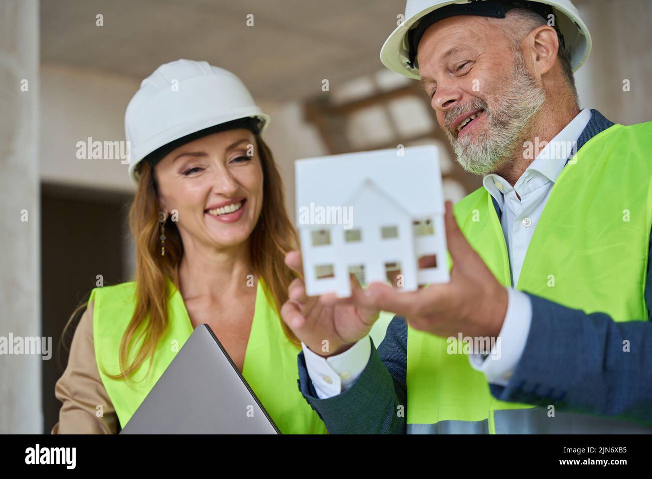 Capataz feliz y agente inmobiliario mirando pequeño modelo de casa Foto de stock