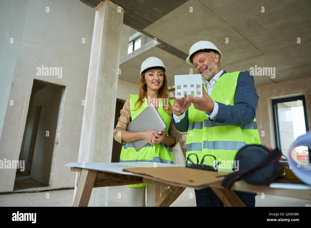 Alegre capataz mostrando agente inmobiliario con computadora portátil en casa miniatura de la mano Foto de stock