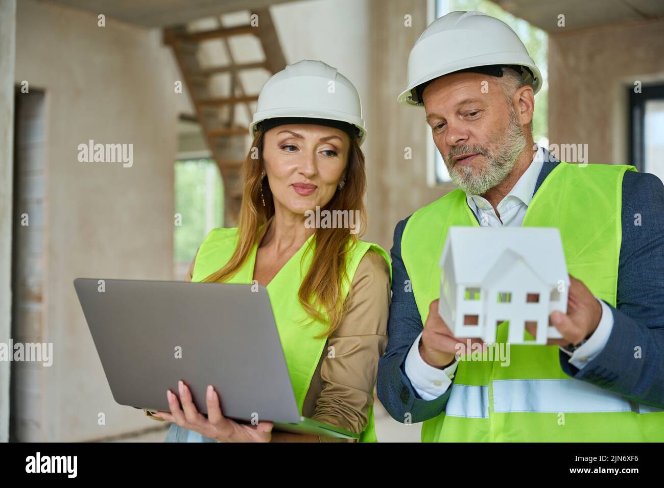 El agente sostiene el ordenador portátil abierto y mira el modelo de la casa Foto de stock