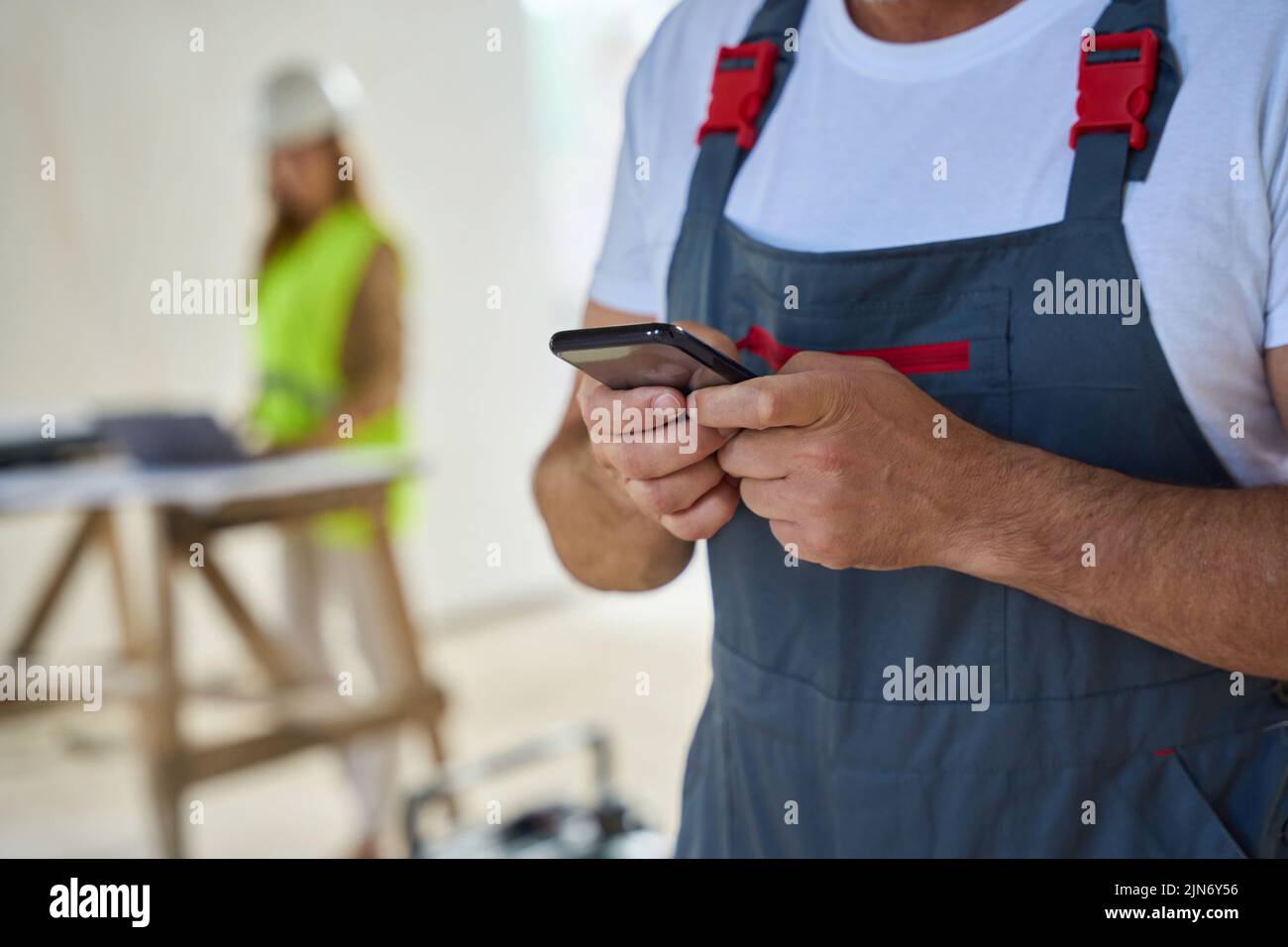 Foto recortada de un trabajador de la construcción escribiendo un mensaje por teléfono Foto de stock