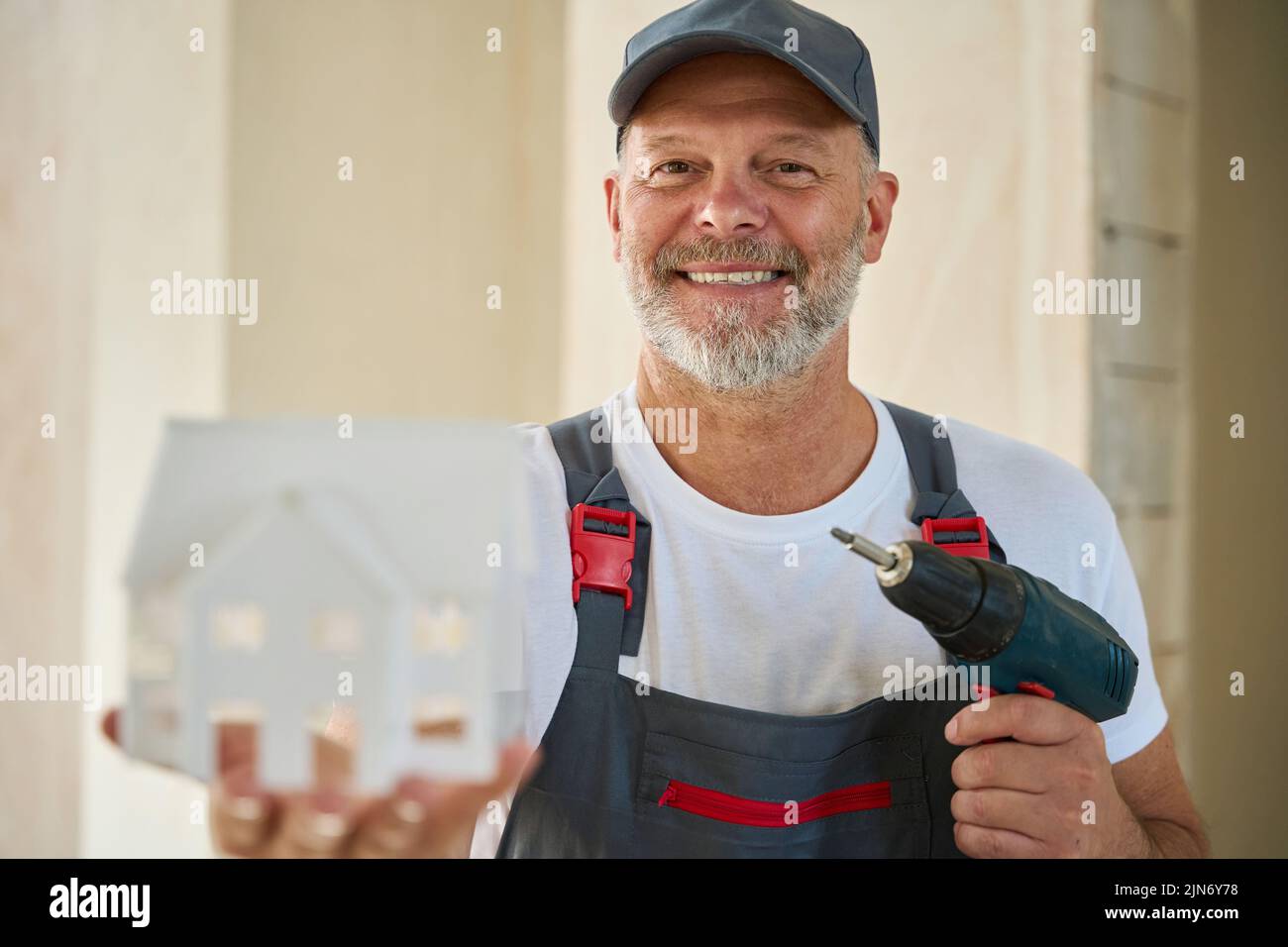 Foto de un constructor adulto sonriente sosteniendo modelo de casa y taladro Foto de stock