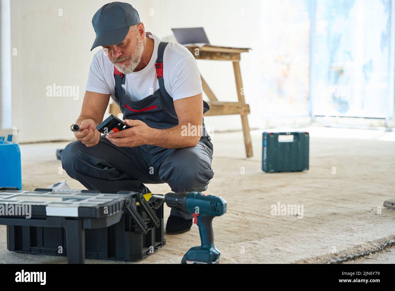 Constructor enfocado mirando sentado cerca de la caja de herramientas y mirando la herramienta Foto de stock