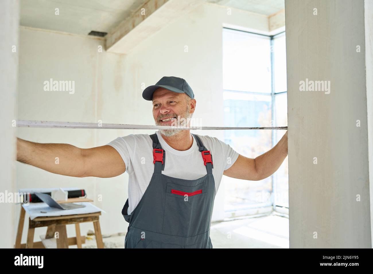 Un trabajador de pelo gris sonriente mide el ancho de la puerta con cinta métrica Foto de stock