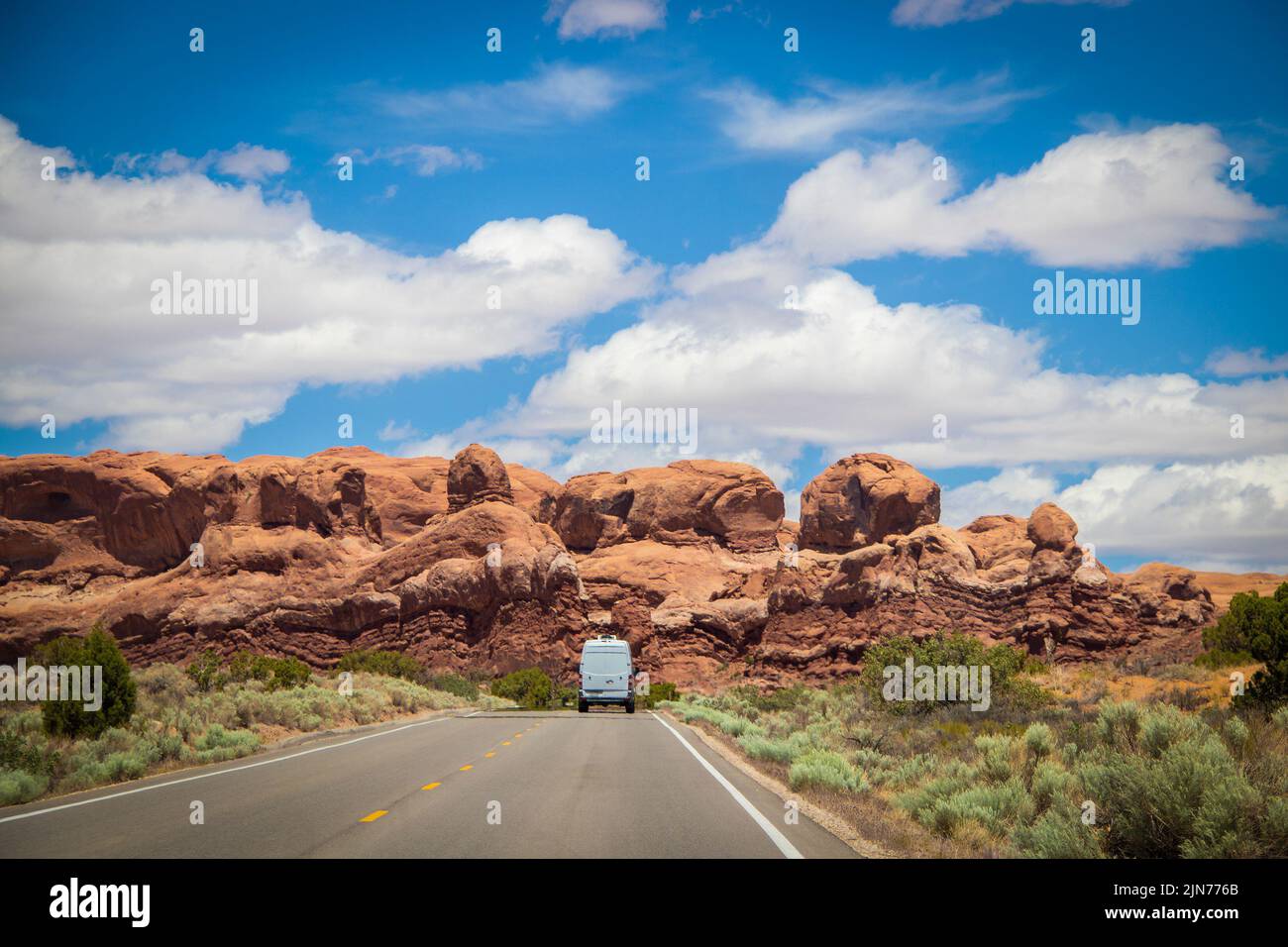 La furgoneta campista blanca conduce hacia la formación de roca roja en el Parque Nacional Arches en Utah, EE.UU. Foto de stock