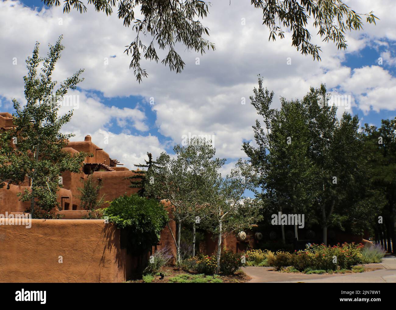 Arquitectura de adobe del suroeste bajo un cielo azul con suaves nubes blancas y rodeado y enmarcado por árboles Foto de stock