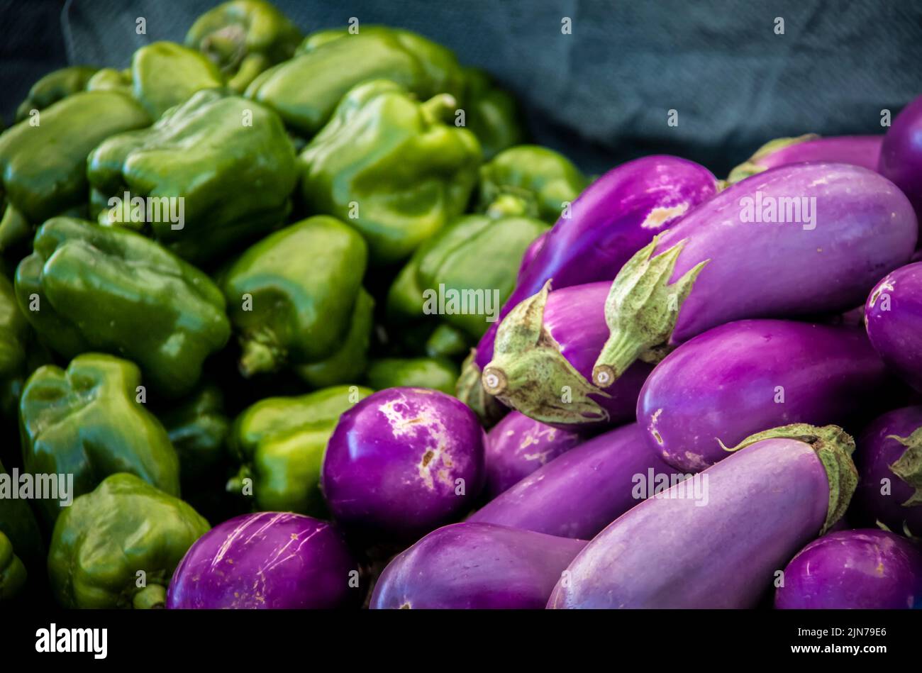 Pila de berenjenas con pimientos verdes dulces bokeh detrás de ellos en el mercado. Foto de stock